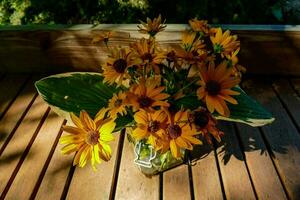 ein Vase von Gelb Blumen Sitzung auf ein hölzern Deck foto