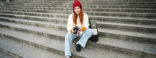 jung Student, Fotograf sitzt auf Straße Treppe und prüft ihr Schüsse auf Fachmann Kamera, nehmen Fotos draußen