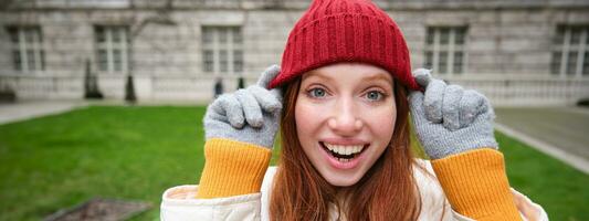 süß Mädchen Schüler im rot Hut, warm Handschuhe, sitzt im Park, lächelt und sieht aus glücklich. foto