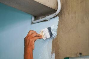 Nahansicht Hand von das Maler halten ein Farbe Bürste Gemälde Weiß Farben auf das Mauer im Renovierung von alt Haus. foto