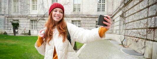 Porträt von glücklich Mädchen Tourist, nimmt Selfie auf Smartphone im Vorderseite von historisch Gebäude, posieren zum Foto auf Handy, Mobiltelefon Telefon Kamera