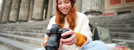 jung Student, Fotograf sitzt auf Straße Treppe und prüft ihr Schüsse auf Fachmann Kamera, nehmen Fotos draußen