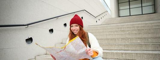 schön Mädchen Tourist sitzt auf Treppe mit Stadt Karte, Pläne ihr Reise, sieht aus zum Richtung während Reisen um Stadt, sucht Route zum Besichtigung foto