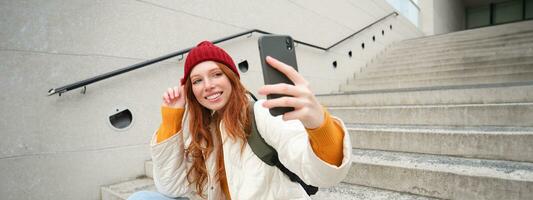 städtisch Mädchen nimmt Selfie auf Straße Stufen, Verwendet Smartphone App zu nehmen Foto von Sie selber, posiert zum Sozial Medien Anwendung