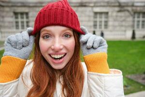 süß Mädchen Schüler im rot Hut, warm Handschuhe, sitzt im Park, lächelt und sieht aus glücklich. foto