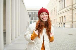 weiblich Tourist im rot Hut mit Rucksack, Besichtigung, erforscht historisch Sehenswürdigkeiten auf ihr Ausflug um Europa, lächelnd und posieren auf Straße foto