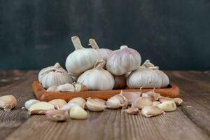 ein groß Kopf von Knoblauch Lügen auf ein hölzern Teller auf ein schwarz Hintergrund. foto