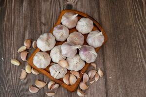 ein groß Kopf von Knoblauch Lügen auf ein hölzern Teller auf ein schwarz Hintergrund. foto