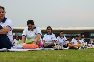 Neu Delhi, Indien, Juni 21, 2023 - - Gruppe Yoga Übung Session zum Menschen beim Yamuna Sport Komplex im Delhi auf International Yoga Tag, groß Gruppe von Erwachsene Teilnahme Yoga Klasse im Kricket Stadion foto