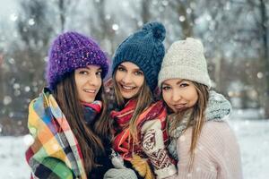 drei Frauen freunde draußen im gestrickt Hüte haben Spaß auf ein schneebedeckt kalt Wetter. Gruppe von jung weiblich freunde draußen im Winter Park. foto