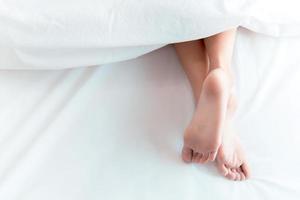 Frauenfüße auf dem Bett unter weißer Decke. Schlaf- und Entspannungskonzept. Urlaub und Urlaubsthema foto