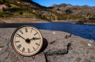 ein Uhr Sitzung auf ein Felsen in der Nähe von ein See foto