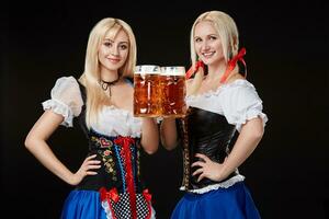 zwei schön blond Frauen sind halten Brille von Bier im Hände und Stand auf schwarz Hintergrund im Studio. foto