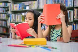 Zwei kleine süße Mädchen, multiethnische Freunde, die zusammen Bücher in der Schulbibliothek lesen. Menschen Lebensstil und Bildung Lernkonzept. glückliche Freundschaftskinder, die Freizeitbeschäftigung für Prüfungstest machen foto