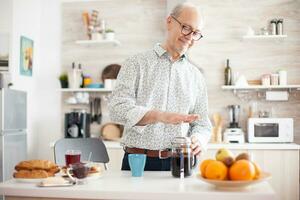 Senior Mann Herstellung Kaffee mit verwenden von ein Französisch Drücken Sie während Frühstück im Küche. Alten Person im das Morgen genießen frisch braun Cafe Espresso Tasse Koffein von Jahrgang Becher, Filter entspannen Erfrischung foto