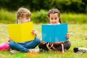 zwei ziemlich Schulmädchen sitzen mit Bücher draußen im das Park. Schulmädchen oder Studenten sind unterrichtet Lektionen im Natur. foto