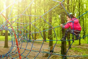 glückliches kleines Mädchen in einem Seilpark auf dem Holzhintergrund foto