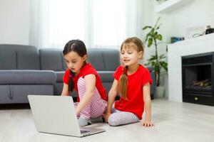 zwei wenig Mädchen Sitzung im Vorderseite von ein Laptop und Lachen, Nahaufnahme, positiv Emotionen, Unterhaltung auf das Internet zum Kinder foto