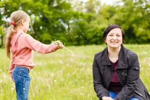 Mutter mit kleiner Tochter weht zu Löwenzahn - Lebensstil im Freien Szene im Park foto