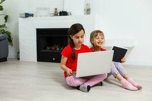 zwei wenig Mädchen Sitzung im Vorderseite von ein Laptop und Lachen, Nahaufnahme, positiv Emotionen, Unterhaltung auf das Internet zum Kinder foto