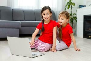 zwei wenig Mädchen Sitzung im Vorderseite von ein Laptop und Lachen, Nahaufnahme, positiv Emotionen, Unterhaltung auf das Internet zum Kinder foto