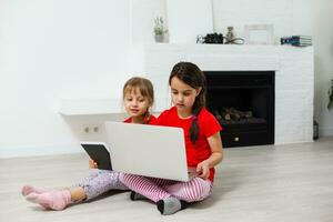 zwei wenig Mädchen sind spielen mit Laptop im Spielzimmer beim Zuhause foto