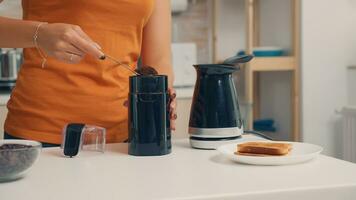 Hausfrau Putten Kaffee im elektrisch Topf während Frühstück. Hausfrau beim Zuhause Herstellung frisch Boden Kaffee im Küche zum Frühstück, Trinken, Mahlen Kaffee Espresso Vor gehen zu Arbeit foto