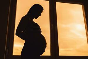 schwanger Frau Stehen neben Fenster und halten ihr Bauch. Silhouette von schwanger Frau. foto