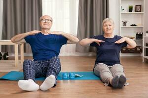 älter Menschen Wer haben ein gesund Lebensstil tun Sport im Leben Zimmer. alt Person gesund Lebensstil Übung beim heim, trainieren und Ausbildung, Sport Aktivität beim Zuhause auf Yoga Matte. foto