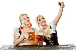zwei schön Frauen halten ein Glas von Bier während Sitzung beim ein hölzern Tabelle auf ein Weiß Hintergrund im das Studio foto