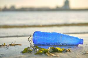 benutzt Blau Glas Flasche Lügen auf das Fluss Bank, Nächster zu das Algen. Reinigung oben Müll. Flussufer Verschmutzung. Freiwilligenarbeit Konzept. Nahansicht Schuss. foto