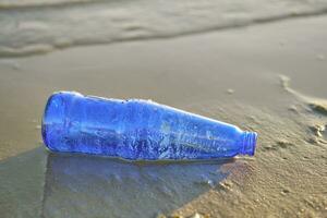 benutzt Blau Glas Flasche Lügen auf das Fluss Bank, Nächster zu das Algen. Reinigung oben Müll. Flussufer Verschmutzung. Freiwilligenarbeit Konzept. Nahansicht Schuss. foto