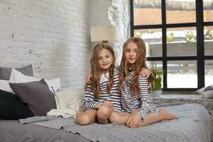 das Bild von zwei wenig Schwestern Sitzung auf das Bett im das Zimmer. foto