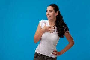 Studio Porträt von ein jung schön Frau im ein Weiß T-Shirt gegen ein Blau Mauer Hintergrund. Menschen aufrichtig Emotionen. foto