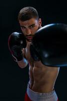 Porträt von zäh männlich Boxer posieren im Boxen Haltung gegen schwarz Hintergrund. foto