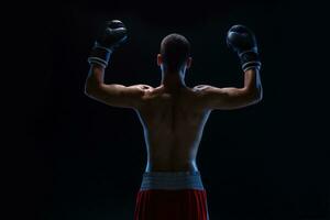 zurück Aussicht von Mann Boxer mit angehoben Hände im Sieg Geste. Konzept von schwer Sport, Ruhm und Erfolg. foto