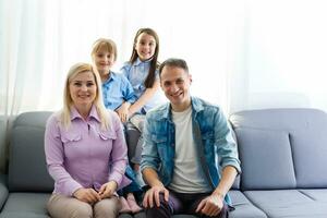 heiter jung Familie mit Kinder Lachen Sitzung auf Couch zusammen, Eltern mit Kinder genießen unterhaltsam beim Zuhause foto