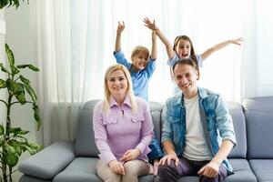 heiter jung Familie mit Kinder Lachen Sitzung auf Couch zusammen, Eltern mit Kinder genießen unterhaltsam beim Zuhause foto