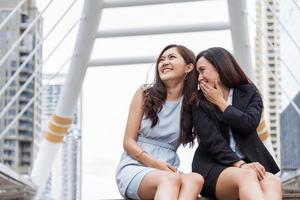 Zwei asiatische Geschäftsfrauen klatschen Witzgeschichte in der Stadt im Freien, nachdem sie die Arbeit beendet haben. Geschäftsfrauen Mitarbeiter und Freundschaftskonzept. Schöne Geschäftsleute, die im Büroleben ein geheimes Skandalthema sprechen