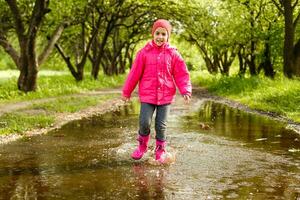 süß wenig Mädchen tragen Regen Stiefel Springen in ein Pfütze foto