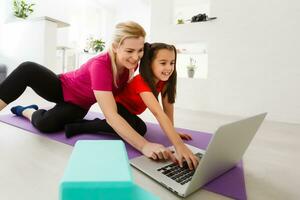 Mutter und Tochter üben online Yoga Lektion beim Zuhause beim Quarantäne Isolierung Zeitraum während Coronavirus Pandemie. Familie tun Sport zusammen online von heim. gesund Lebensstil foto