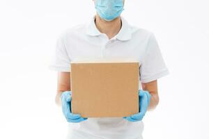 Zuhause Lieferung, online Befehl. ein Mann im Uniform, ein medizinisch Maske und Gummi Handschuhe mit ein Kasten, ein Paket im seine Hände. Essen und Essen Lieferung während das Quarantäne von das Coronavirus Pandemie foto