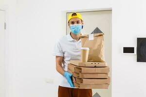 Mann von Lieferung Bedienung im T-Shirt, im schützend Maske und Handschuhe geben Essen bestellen und halten Pizza Kisten Über Weiß Hintergrund foto