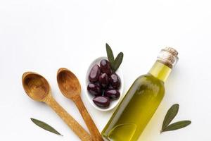 Olivenölflasche, lila Oliven und Holzlöffel foto