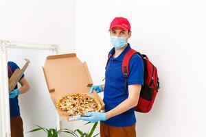 Lieferant mit schützend medizinisch Maske halten Pizza Box - - Tage von Viren und Pandemie, Essen Lieferung zu Ihre heim. foto