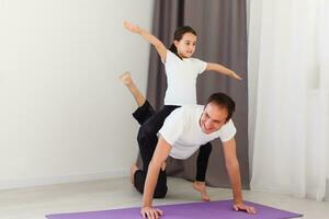 gut aussehend jung Vater und seine süß wenig Tochter sind tun respektieren Planke mit Bein erziehen auf das Fußboden beim heim. Familie Fitness trainieren. foto