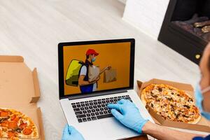 Mann im schützend Handschuhe und Maske mit Laptop zum online Essen bestellen während Quarantäne, Nahaufnahme. Lieferung Bedienung foto