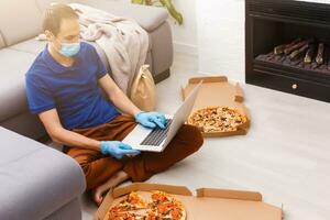 Mann im schützend Handschuhe und Maske mit Laptop zum online Essen bestellen während Quarantäne, Nahaufnahme. Lieferung Bedienung foto