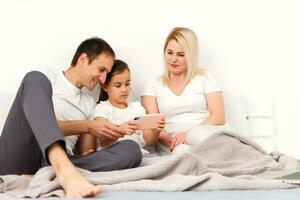 Familie Lügen im Bett zusammen mit Digital Geräte foto