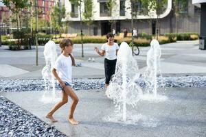 glücklich Teenager Mädchen Tanzen im ein Brunnen im ein Stadt Park auf ein heiß Sommer- Tag. foto